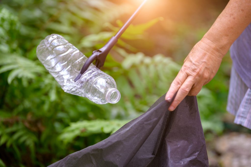 Closeup of hand and waste grabber picking up drinking plastic bottle waste into bag.