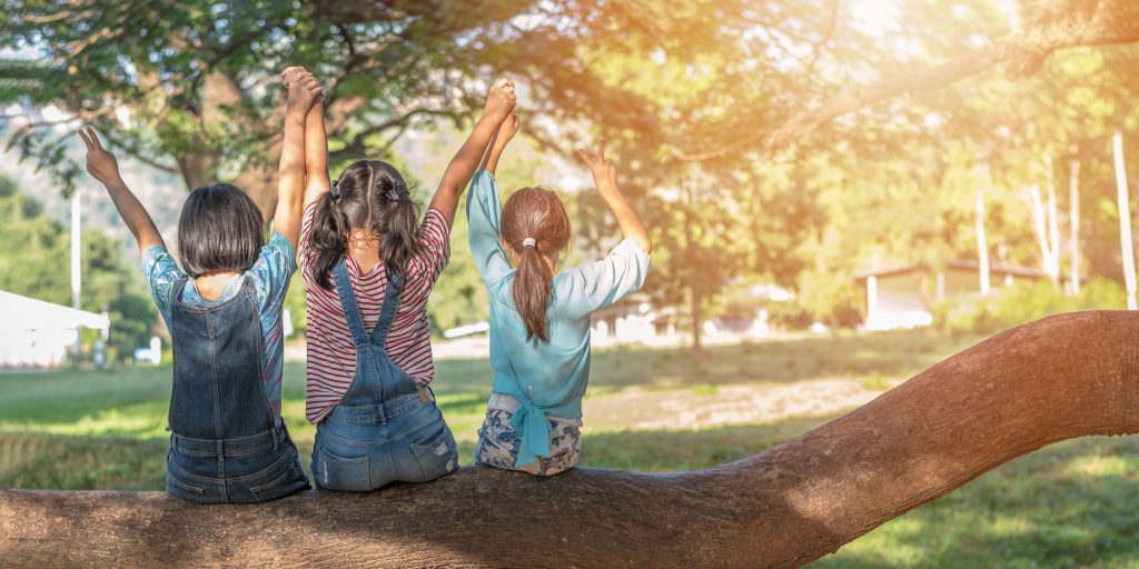 Children friendship concept with happy girl kids in the park having fun sitting under tree shade playing together